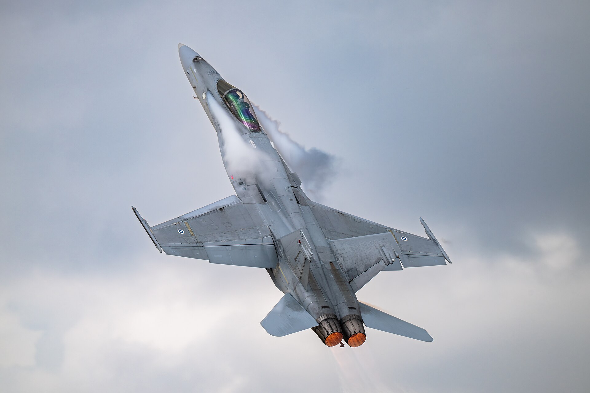 An F/A-18 Hornet performs a high-angle-of-attack manoeuvre during an air show display, with condensation revealing vortices shed from the leading-edge root extensions in humid air. Condensation forms